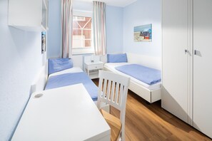 Ein Schlafzimmer mit zwei Einzelbetten, einem Schreibtisch, einem Stuhl, einem Kleiderschrank und einem Fenster mit Vorhängen.