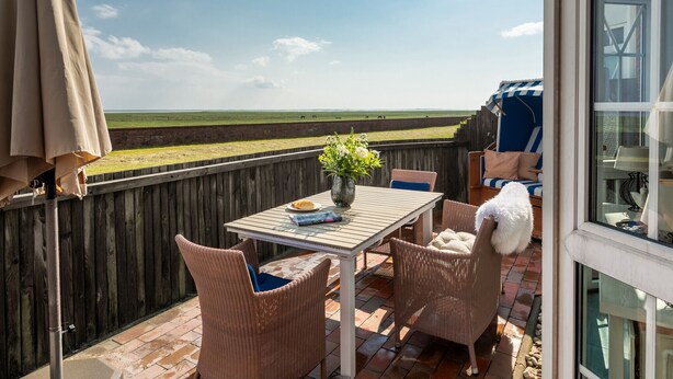 Eine Terrasse mit Korbstühlen, einem Tisch und Blick aufs Meer.