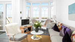 Ein modernes Wohnzimmer mit einer Couch, zwei Sesseln, einem Couchtisch und einem Fernseher.