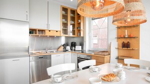 Eine moderne Küche mit Edelstahlgeräten, Holzschränken und einem Essbereich mit weißen Stühlen und einem für Tee gedeckten Tisch.