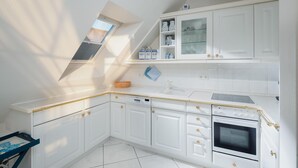 Une cuisine moderne avec des meubles blancs, un four encastré et une lucarne.