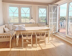Ein Zimmer mit Holztisch und -stühlen, einer Couch und großen Fenstern mit Blick ins Freie.