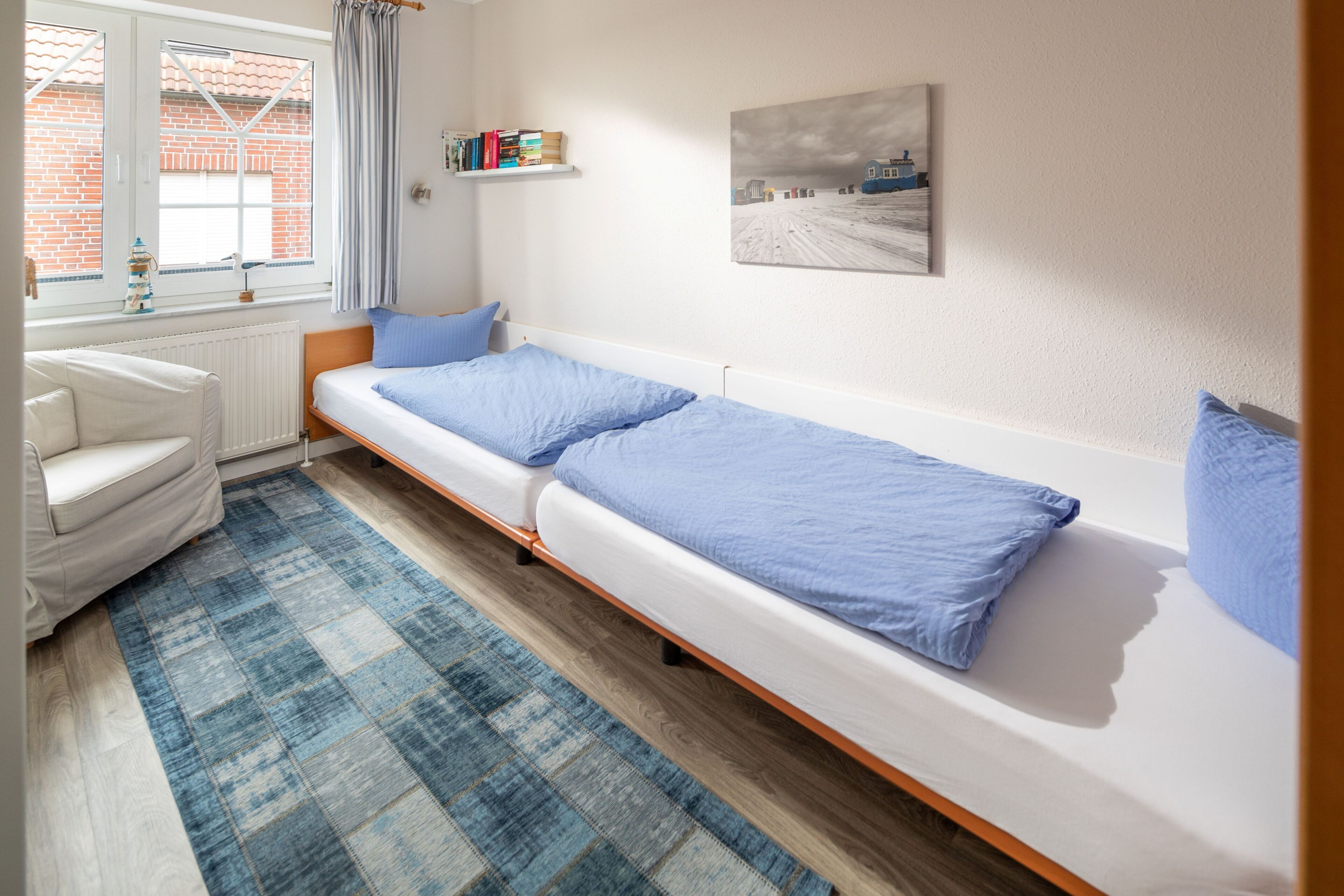 Een kamer met een bed, een stoel, een radiator, een raam met gordijnen, een plank met boeken en een schilderij aan de muur.