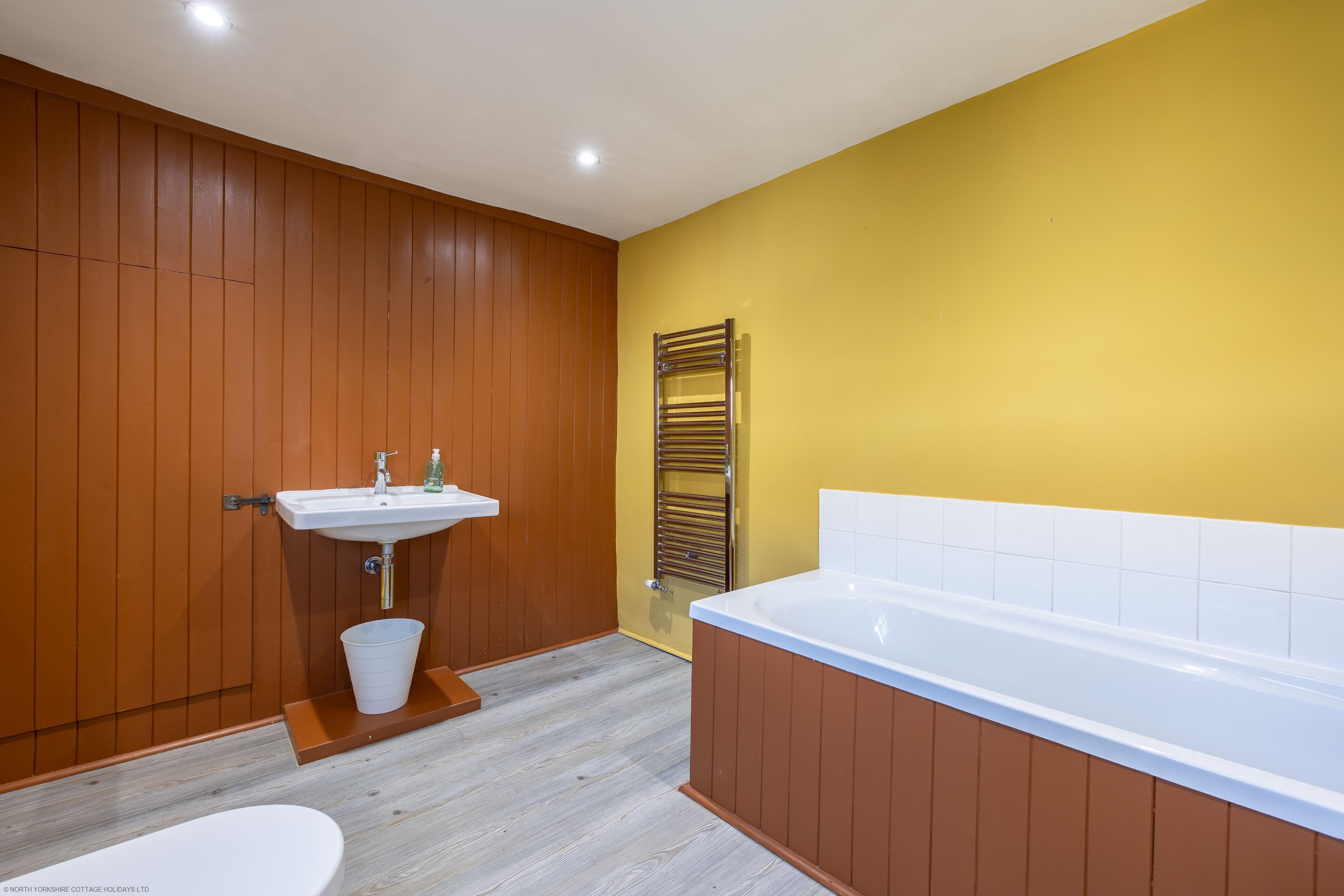 A bathroom with a wooden wall, a white sink, a bathtub, and a toilet.
