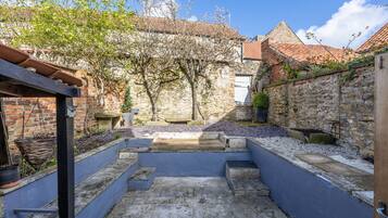 A courtyard with stone walls, a wooden pergola, and a view of a building with a tiled roof.