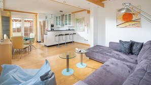 Un salon moderne avec un canapé, une table basse en verre et une cuisine en arrière-plan.