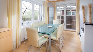Une cuisine moderne avec une table à manger en verre, des chaises de couleur claire et une vue dégagée grâce à de grandes fenêtres.