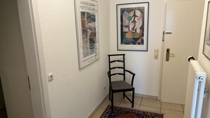 Ein Flur mit einem Sessel, zwei gerahmten Kunstwerken, einer Heizung und einer Tür.