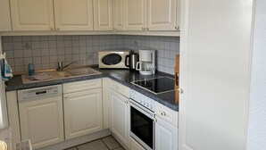 Eine kleine Küche mit weißen Schränken, einer Mikrowelle, einer Kaffeemaschine, einem Geschirrspüler und einem Backofen.