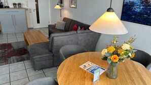 Ein Wohnzimmer mit grauem Sofa, einem Holztisch, einer Blumenvase und einer Lampe.