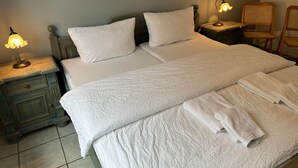 Ein ordentlich gemachtes Bett mit weißen Leinen und Kissen, eine Nachttischlampe, ein Holznachttisch und ein Stuhl.