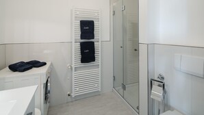 Un baño moderno con cabina de ducha de vidrio, lavadora blanca y un perchero con toallas.