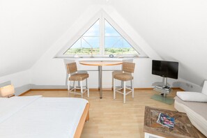 Un dormitorio con cama, escritorio con dos sillas, televisor y ventana con vistas.