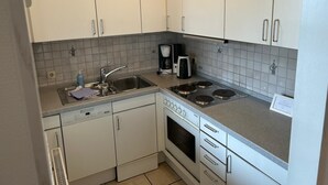 Ett kompakt kök med vita skåp, en inbyggd diskmaskin, en kaffebryggare och en spis.