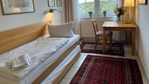 Ett rum med en säng, ett skrivbord, en stol, ett fönster med gardiner och ett element.