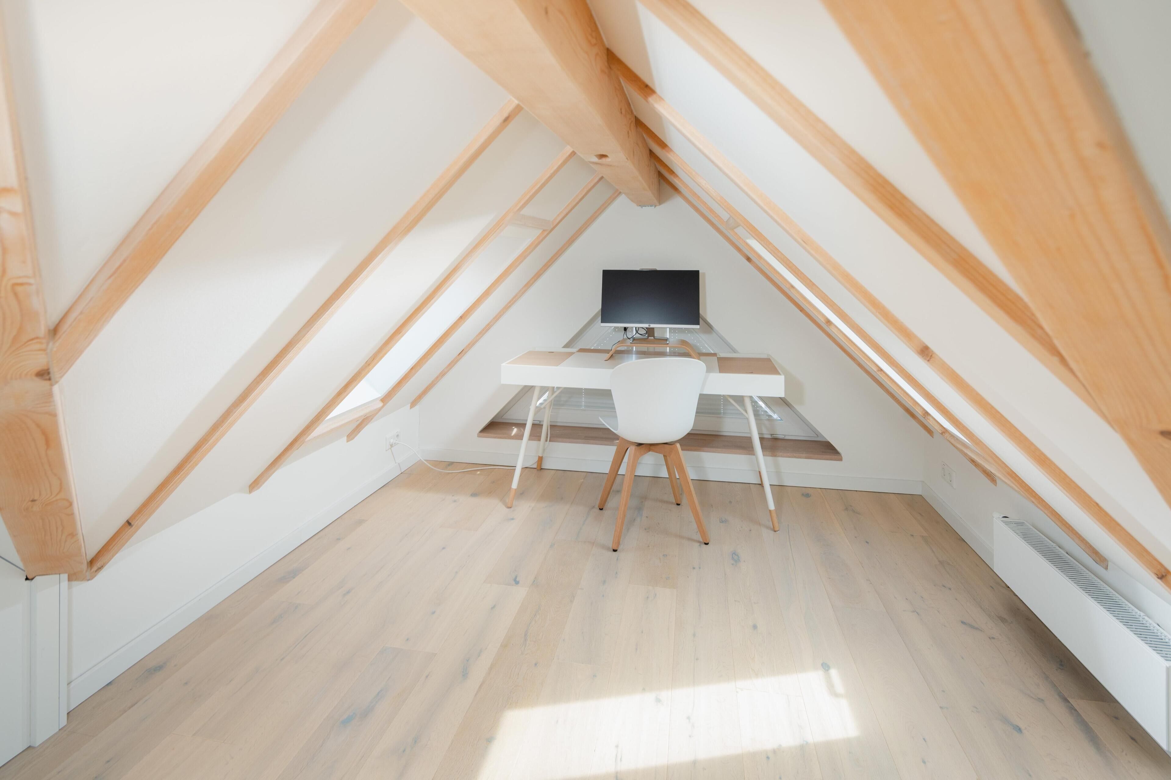 Ein Dachzimmer mit Schreibtisch, Stuhl und Computer.