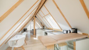 Una cocina estilo altillo con vigas de madera, un comedor con sillas blancas y una isla de cocina.