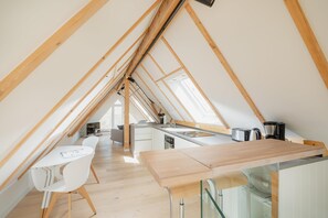 Eine Dachküche mit Holzbalken, ein Essbereich mit weißen Stühlen und einer Kücheninsel.