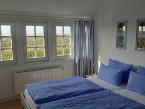 A bedroom with a bed, a radiator, three windows, and a curtain. - Vacation apartment in Landhaus Bant (Juist)