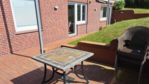 A patio area with a table and chair, a brick building in the background, and a grassy area. - Vacation apartment Bootjefahrt at Uns to Hus (Juist)