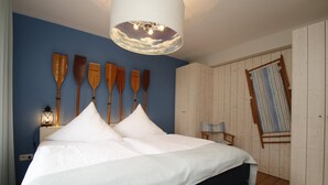 A bedroom with a bed, wooden wall decorations, a ceiling light, a nightstand, and a window with a view. - Vacation apartment Bootjefahrt at Uns to Hus (Juist)