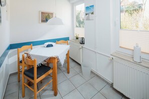 A small dining area with a table and chairs, a radiator, a window with blinds, and a wall-mounted picture. - Frauke apartment in the Villa Altmanns (Juist)