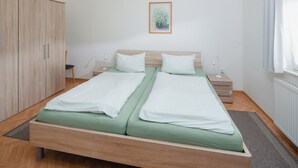 Een tweepersoonsbed met groene beddengoed, een houten garderobe, een nachtkastje met een lamp, en een ingelijste foto aan de muur.