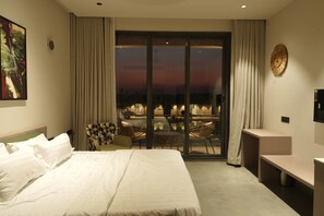 A hotel room with a bed, a dining area with chairs and a table, and a view through a glass door. - Ramee Vanam Resort Sasan Gir (Mendarda)