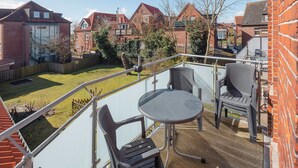Ein Balkon mit Tisch und Stühlen, eine Holzterrasse und Blick auf eine Wohngegend mit Häusern.
