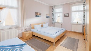 Ein Schlafzimmer mit Bett, Nachttischen, einem Fenster mit Vorhängen, einer Heizung und einem kleinen Bild an der Wand.