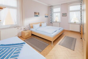 A bedroom with a bed, bedside tables, a nightstand, a window with curtains, a radiator, and a small picture on the wall. - Peterke apartment in the Villa Altmanns (Juist)