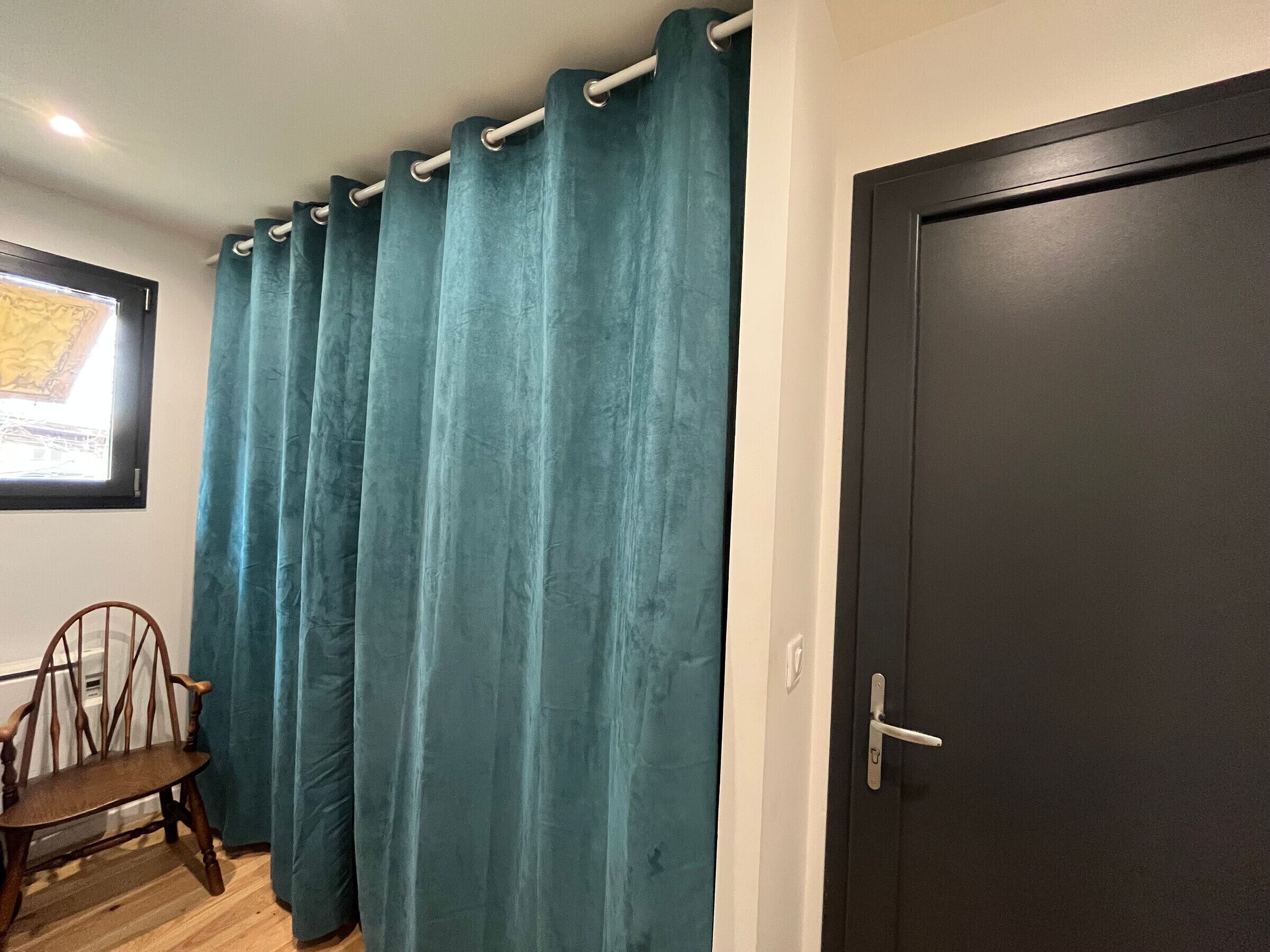A room with a teal curtain, a wooden chair, and a dark door.