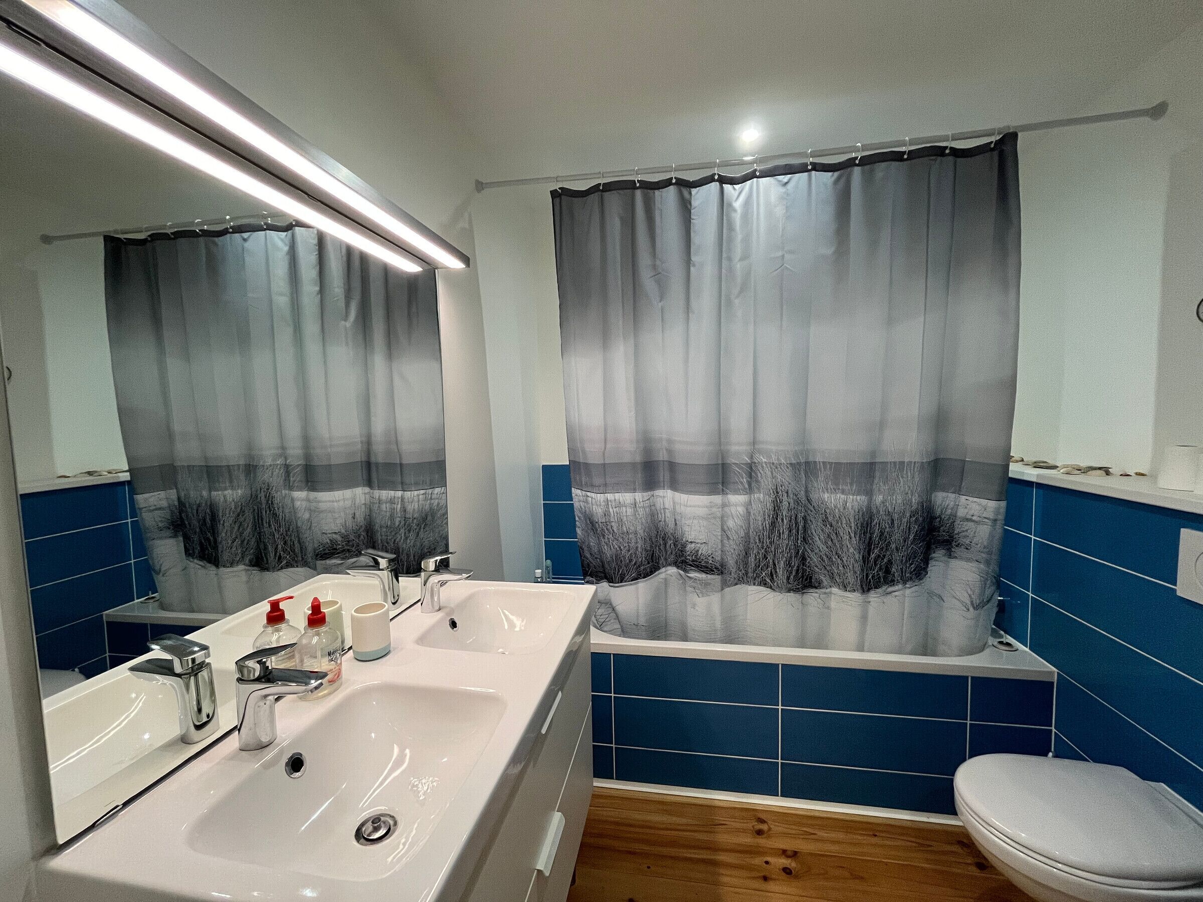 A bathroom with a white sink, two mirrors, a shower curtain, and blue tiles.