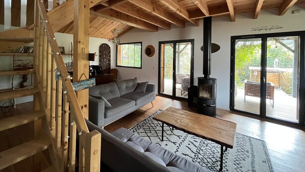 Een houten interieur met een trap, een bank, een tafel en een houtkachel.