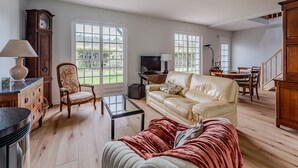Un salon comprenant un canapé, un fauteuil, une table basse, un téléviseur et un coin repas avec des chaises et une table.