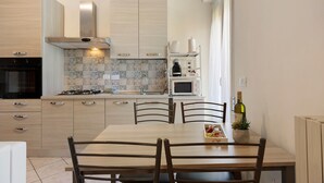 A modern kitchen with wooden cabinets, a gas stove, a microwave, and a dining table with chairs. - Holiday Home Villanova (Villanova)