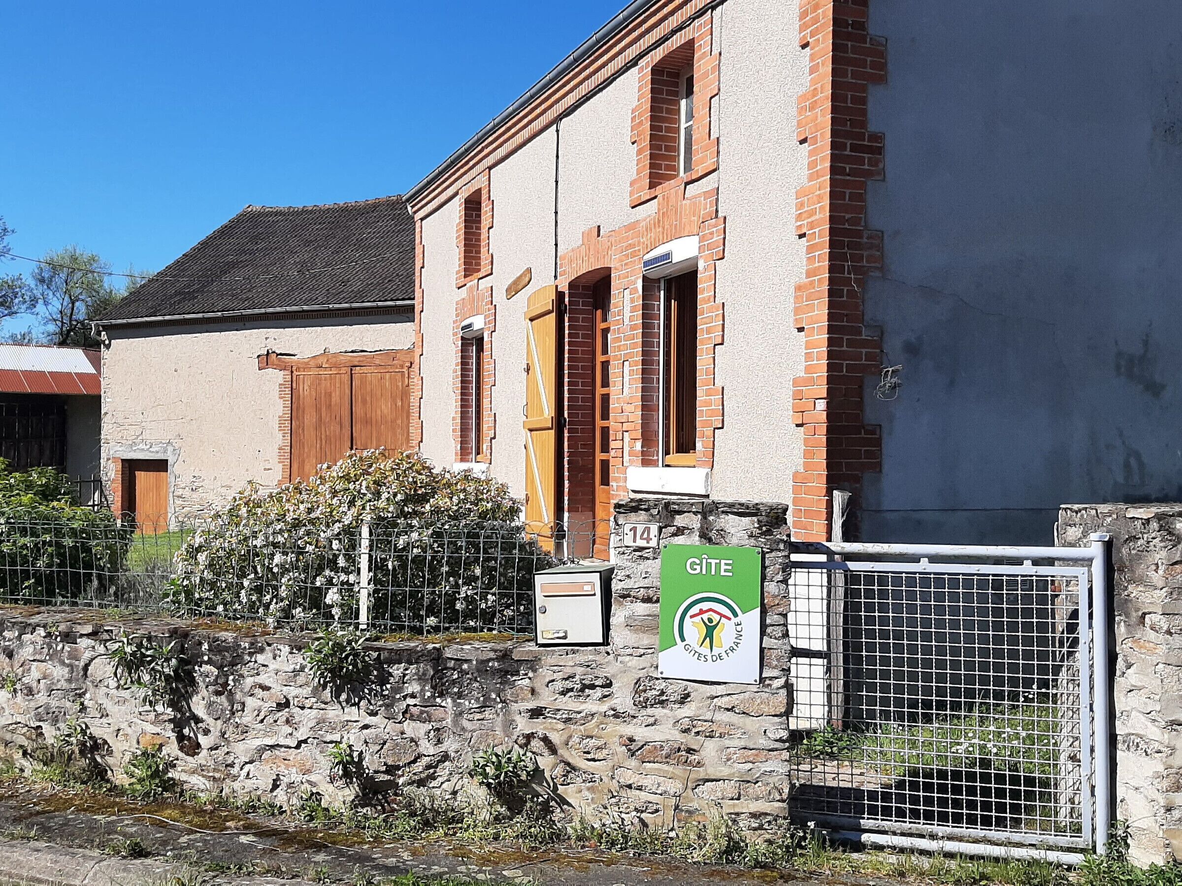 A building with a stone wall, a metal gate, and a green sign with 'GITE' on it.
