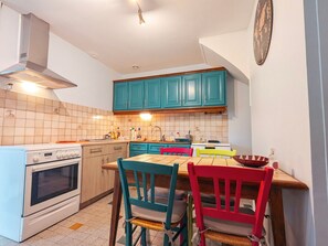 Una cocina con armarios color esmeralda, una estufa blanca y una mesa de comedor con sillas de colores.