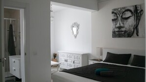 Een slaapkamer met een bed, nachtkastje, kapstok, spiegel en een kunstwerk aan de muur.