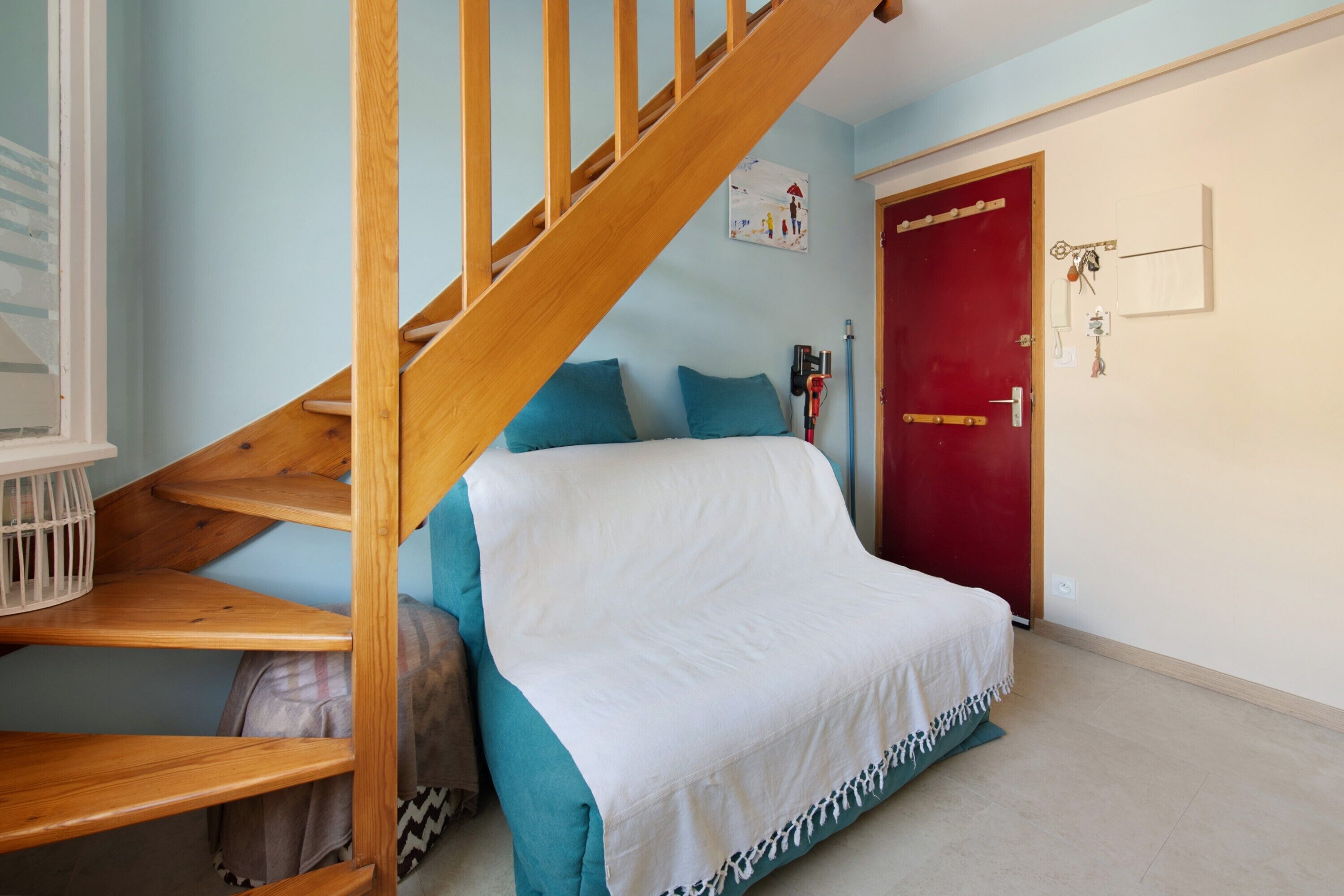 A bedroom with a wooden staircase, a red door, and a bed with a white cover.