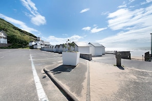 Une route cÎtiÚre bordée de bùtiments blancs, un espace de stationnement et une vue sur la mer.
