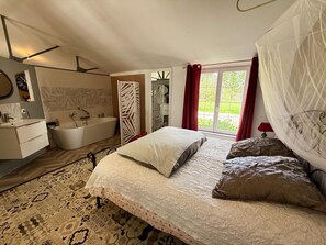 A bedroom with a large bed, a bathtub, a vanity, and a window with a view.
