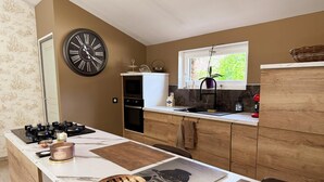 Une cuisine avec une grande horloge murale, une fenêtre donnant sur un espace verdoyant, un évier et une cuisinière.