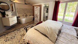 Une chambre à coucher avec un lit, une salle de bain avec une baignoire, un miroir et une fenêtre avec des rideaux.