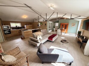 A spacious living area with a sofa, armchairs, a dining table, and a kitchen in the background. - Charming lodging, pets welcome - 2 guests (Cour-Cheverny)