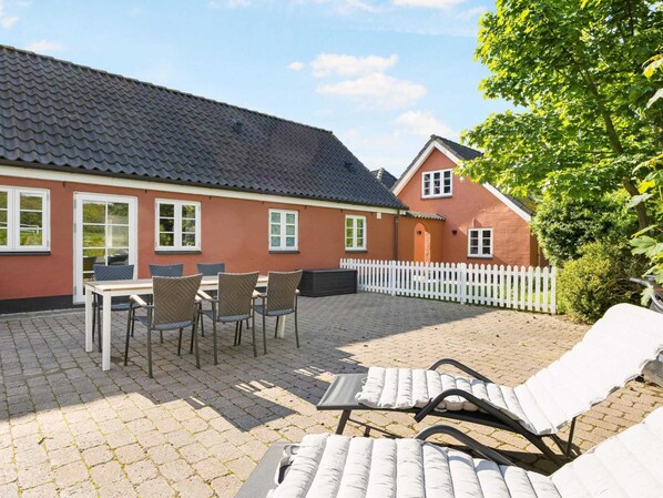A red building with a tiled roof, a white picket fence, and outdoor seating with chairs and tables. - 4 Star Holiday Home in Hjorring (Hjørring)