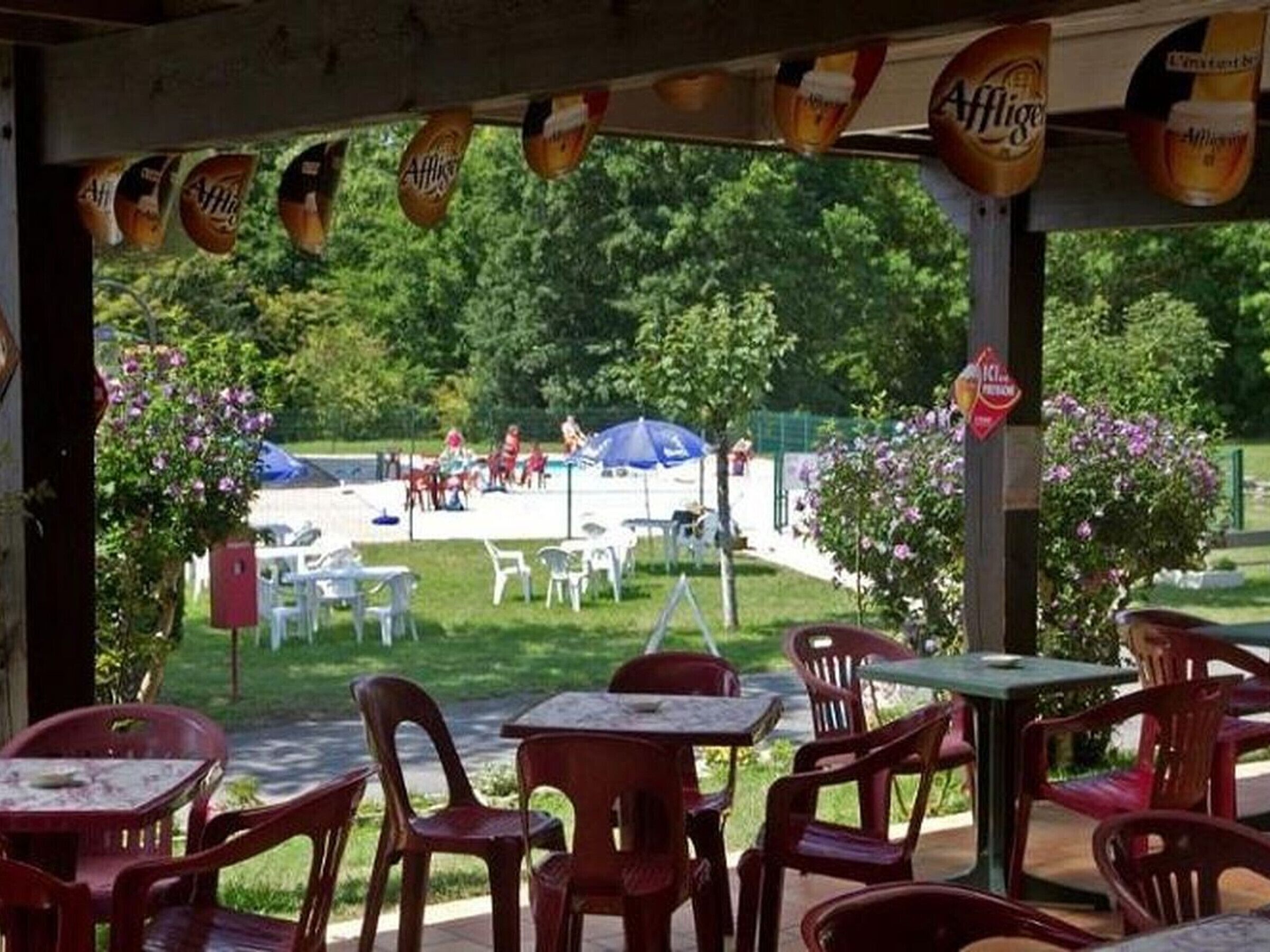 Un área de estar al aire libre con mesas y sillas de plástico, una piscina al fondo y banderines de cerveza.