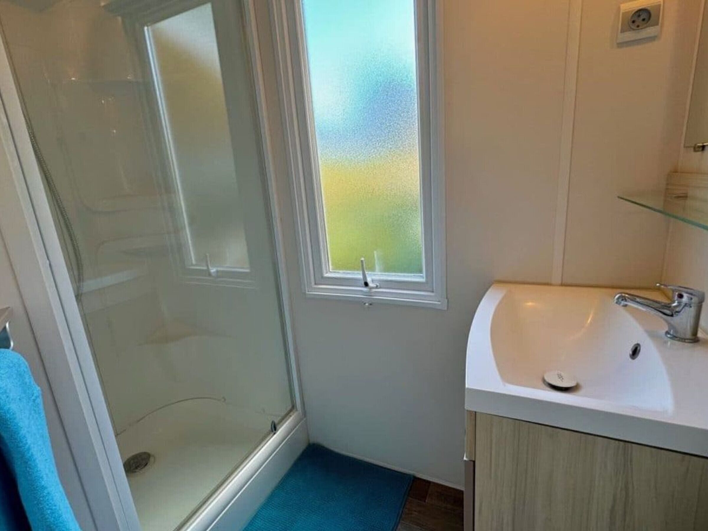A bathroom with a shower, a sink, and a window with frosted glass.