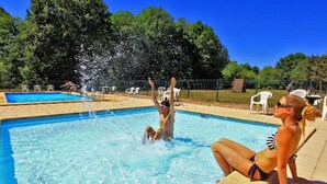 Ein Schwimmbad mit klarem, blauem Wasser, umgeben von Bäumen und einem eingezäunten Bereich mit Liegestühlen.