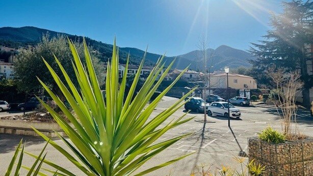 A parking lot with cars, a building, and mountains in the background. - Comfortable apartment near the center - 4 guests (Amélie-les-Bains-Palalda)